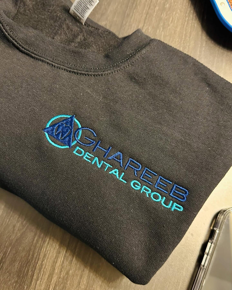 Ghareeb Dental Group logo embroidered in blue and turquoise on a charcoal shirt by The Sovereign Sage.